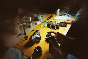 Cologne-Camera-Service-Analog-Technik-Foto Two analog cameras and several lenses on a table, accompanied by hands waiting for equipment.