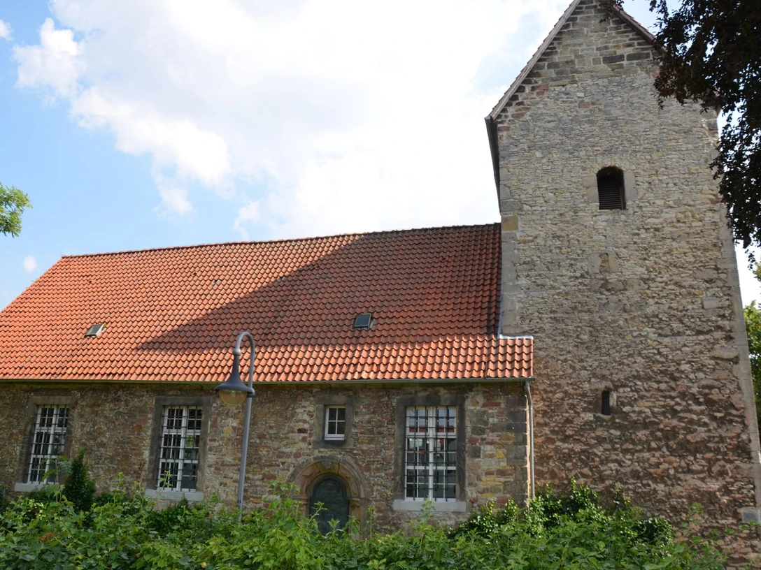 Kniestedter Kirche (10)_HD.JPG Kniestedter Kirche als Steinkirche mit rotem Ziegeldach und Turm, umgeben von Bäumen unter blauem Himmel.