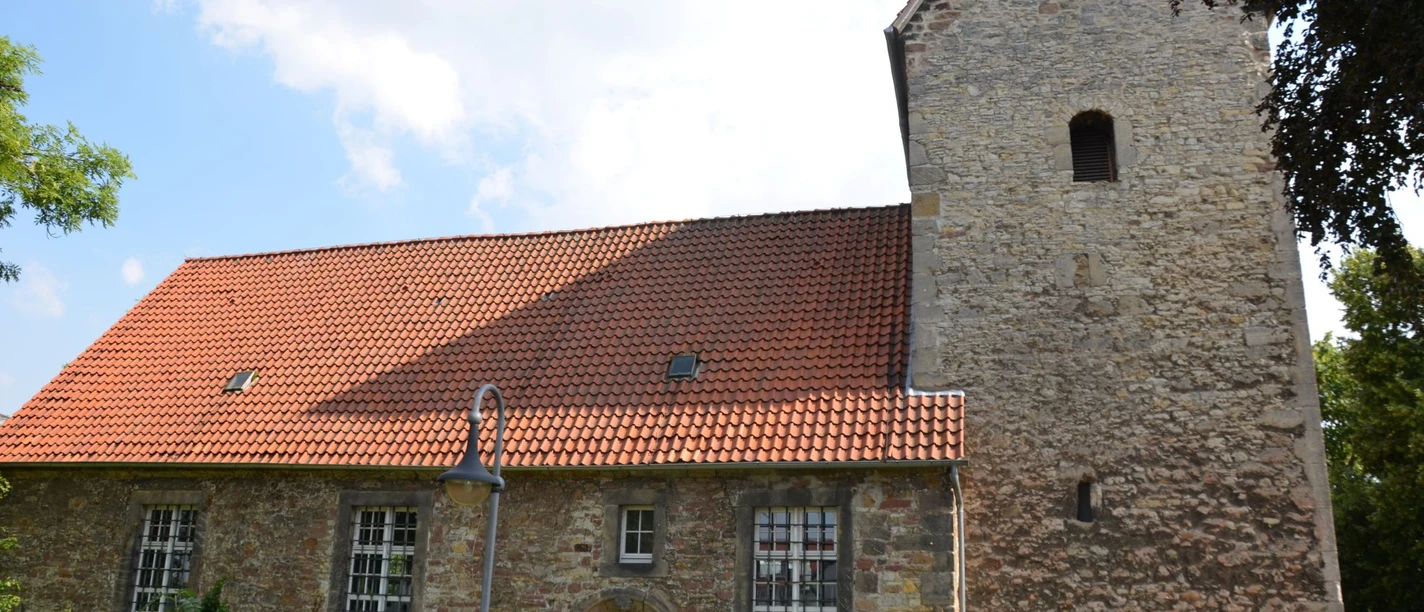 Kniestedter Kirche (10)_HD.JPG Kniestedter Kirche als Steinkirche mit rotem Ziegeldach und Turm, umgeben von Bäumen unter blauem Himmel.