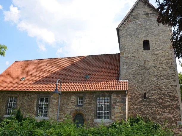 Kniestedter Kirche (10)_HD.JPG Kniestedter Kirche als Steinkirche mit rotem Ziegeldach und Turm, umgeben von Bäumen unter blauem Himmel.