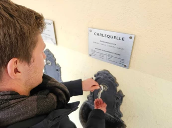 Bad-Driburg Bad Hermmansborn-Quellen-1 Aus einem kunstvoll verzierten Wandbrunnen füllt sich ein Gast der Mineralheilwasser ab.