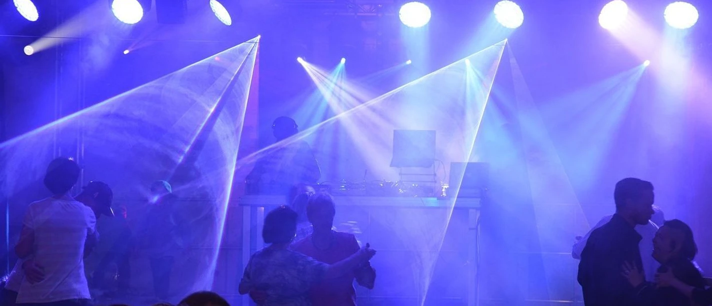 Party Tanzende Menschen unter buntem Licht auf einer Party mit DJ und lebendiger Atmosphäre.