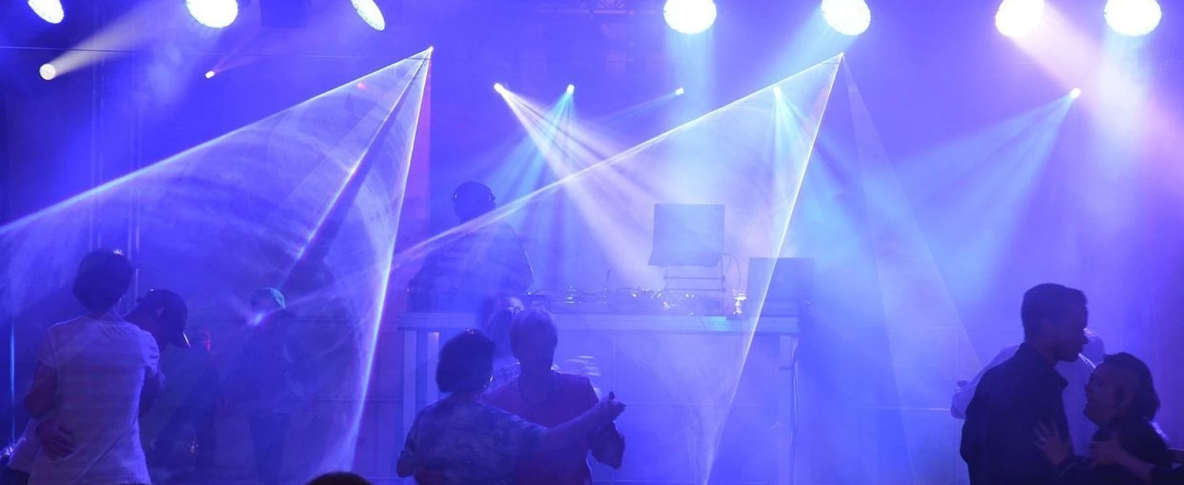 Party Tanzende Menschen unter buntem Licht auf einer Party mit DJ und lebendiger Atmosphäre.