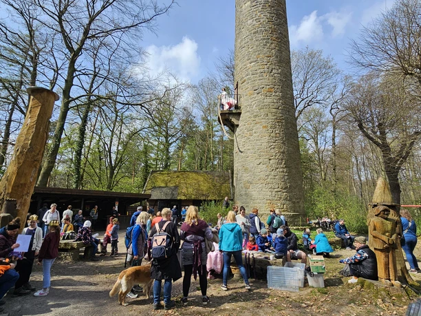 Rapunzel-Turm-Tag Kinder und Erwachsene versammeln sich vor einem steinernen Turm im Wald beim Märchenfest Rapunzel.