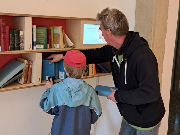 Ausstellung Romantik Bad Rehburg Child and adult in front of a bookshelf in the Romantik Bad Rehburg exhibition