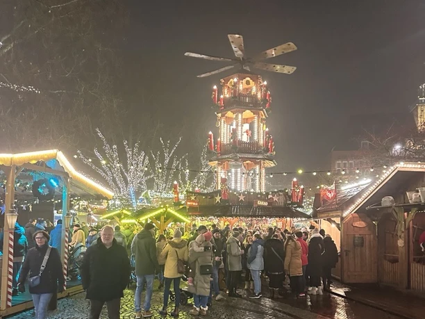 Menschen bummeln über den festlich beleuchteten Engelkemarkt in Emden mit großer Weihnachtspyramide.