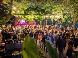 20 Jahre KuK 3 (c) Elke Kohlrautz.jpg Menschenmenge bei einem abendlichen Open-Air-Konzert, umgeben von Bäumen und Lichterketten.