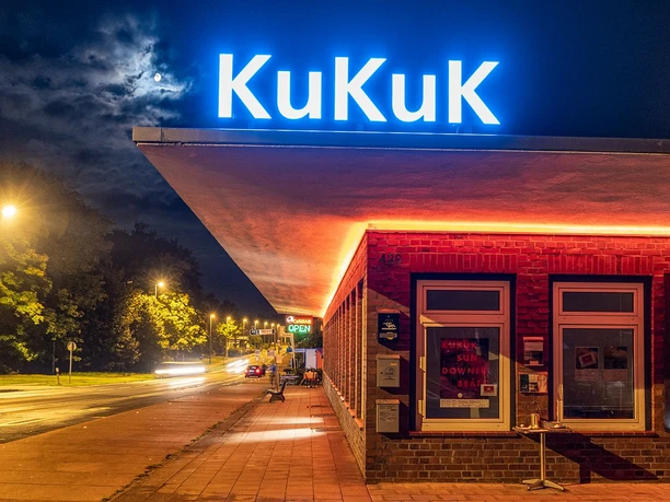 Leuchtende Fassade des Deutschen Zollhauses nachts, mit Neonlicht und beleuchtetem KuKuK-Logo.