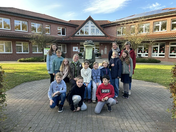 Die Bonis waren einst auch Namensgeber von MOORex.JPEG Kindergruppe und Erwachsene vor rotem Backsteingebäude mit Bronzefigur im Hof bei sonnigem Wetter