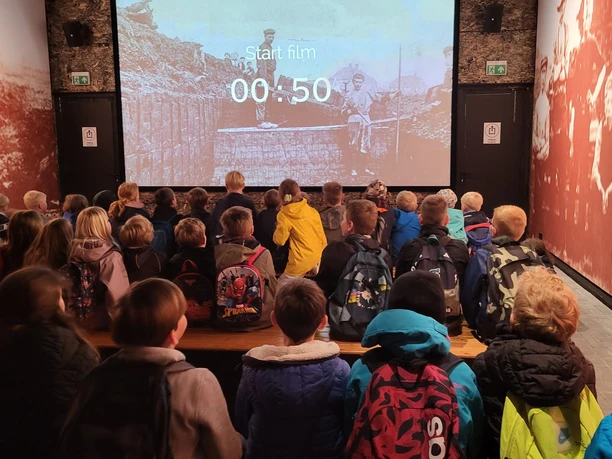 Auf einer großformatigen Leinwand dokumentiert ein historischer Film das Leben der Moorbauern.jpg Kindergruppe mit Rucksäcken sitzt in dunklem Raum und sieht einen historischen Film über Moorbauern