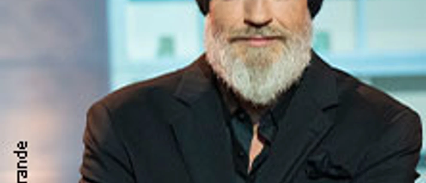 Torsten Sträter mit schwarzer Mütze und Bart vor einer modernen Kulisse.
