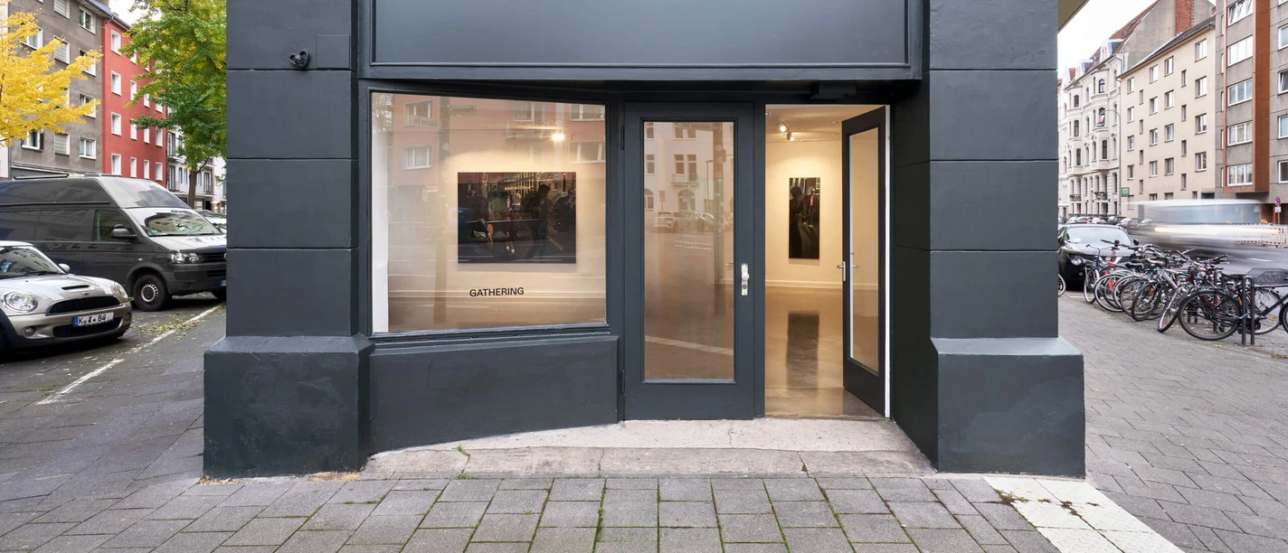 Installationsansicht von Laurie Smith, Brick boys, bei Gathering Cologne Moderner Galerieeingang mit gläserner Fassade und Kunstwerken im Inneren in urbaner Umgebung.