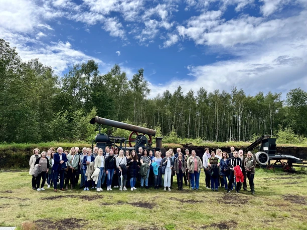Die Teams der Twister Grundschulen auf Exkursion im Moor.JPG Gruppe von Erwachsenen und Kindern steht im Moor vor alter Torfmaschine unter blauem Himmel.