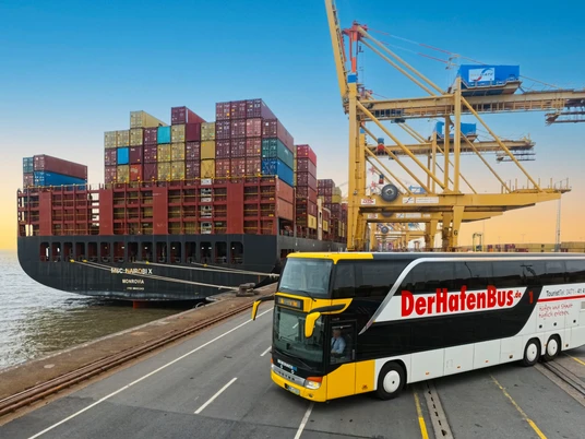 HafenBus IMG_20250411_144835_067 (c) Helmut Gross_Erlebnis Bremerhaven_bearbeitet mit KI_ Ausschnitt.jpg Großes Containerschiff und gelb-weißer Doppelstockbus am Containerterminal in Bremerhaven.