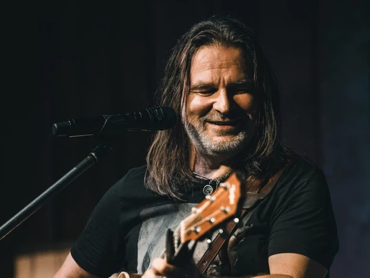 RAY WILSON c by Stefan Strassenburg Ein Musiker mit Gitarre singt auf der Bühne und lächelt während des Auftritts ins Mikrofon.
