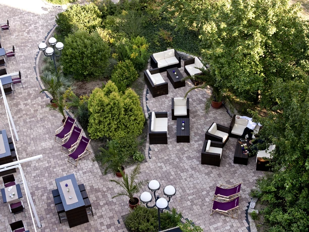 Mercure Hotel & Residenz Frankfurt Messe - Aussenbereich Mischbestuhlung im Außenbereich, umgeben von grünen Büschen und Bäumen.