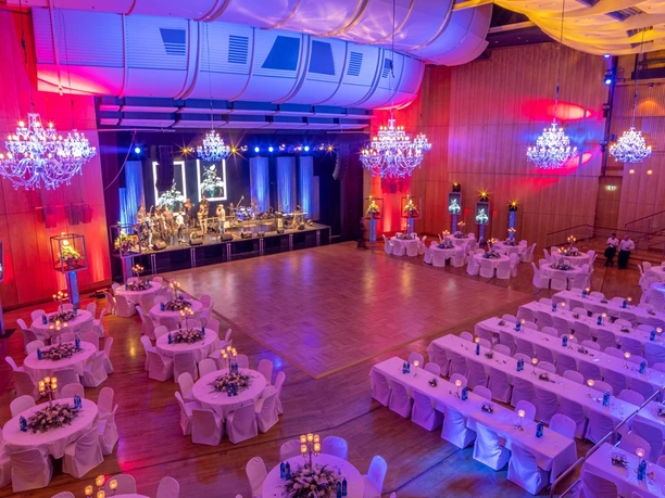 Stadthalle Aschaffenburg - Festsaal Festsaal mit Tischen, Kronleuchtern und Bühne.