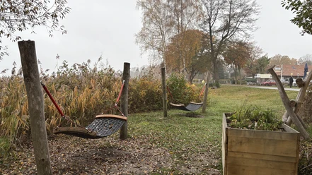 Rastplatz vor dem Naturparkhaus.JPG Holzpfosten mit Netzschaukeln auf einer Wiese vor herbstlicher Vegetation und Häusern im Hintergrund.