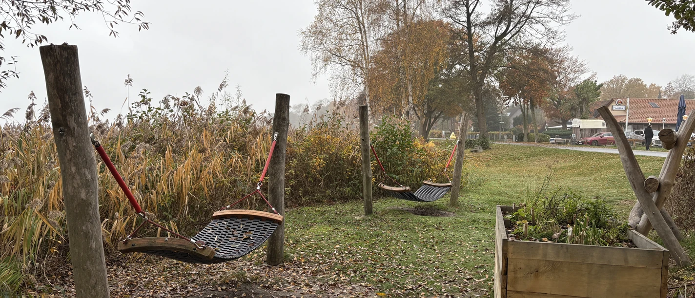 Rastplatz vor dem Naturparkhaus.JPG Holzpfosten mit Netzschaukeln auf einer Wiese vor herbstlicher Vegetation und Häusern im Hintergrund.