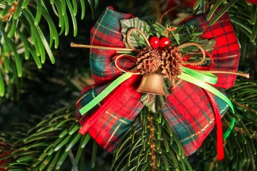 Ein handgefertigter Weihnachtsanhänger aus Tannenzweigen mit rot-grüner Schleife und Glocke.