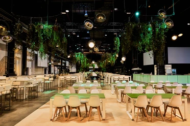 WISAG Event Service GmbH & Co. KG - Ball room A hall with mixed seating, in which green plants hang from the ceiling.