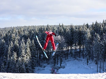 Nordische Kombination Klingenthal_Archiv Sparkasse Vogtland Vermarktungsgesellschaft (6).jpg Ein Skispringer im roten Anzug fliegt über eine schneebedeckte Landschaft.A ski jumper in a red suit flies over a snow-covered landscape.Nad zasněženou krajinou letí skokan na lyžích v červené kombinéze.Skoczek narciarski w czerwonym kombinezonie przelatuje nad zaśnieżonym krajobrazem.Een skispringer in een rood pak vliegt over een besneeuwd landschap.Uno sciatore in tuta rossa vola su un paesaggio innevato.
