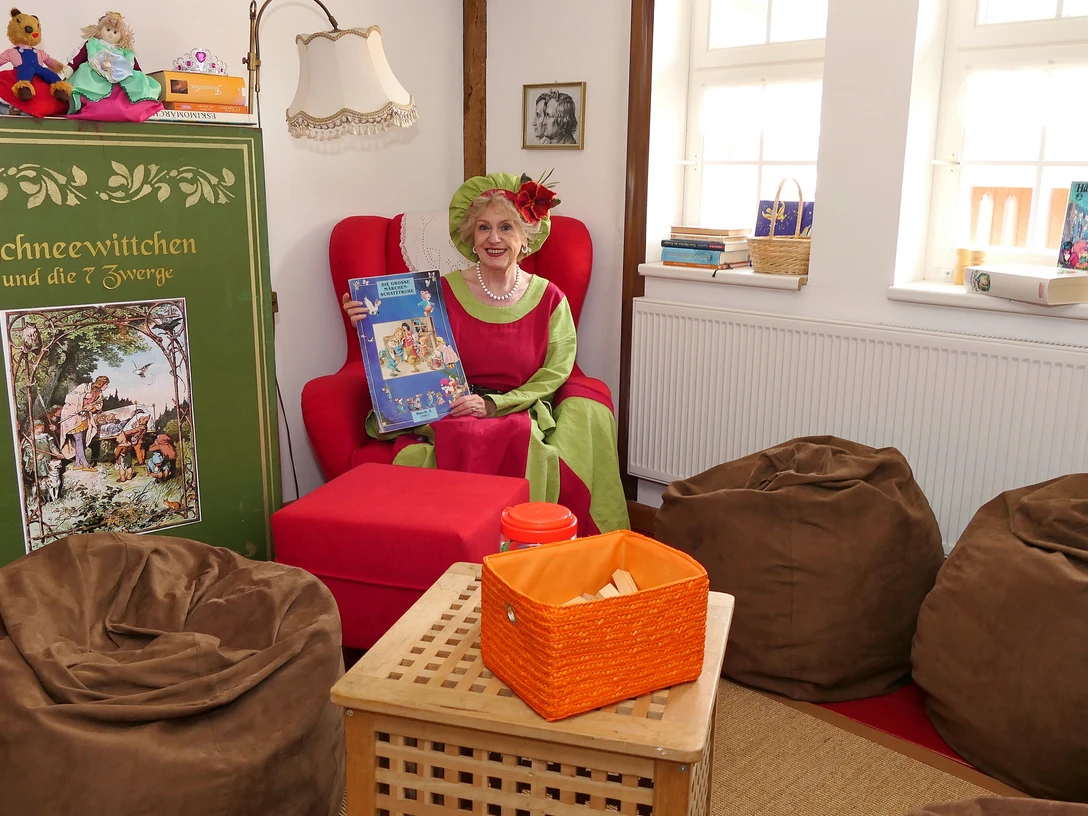 Eine Frau sitzt in einem roten Sessel und hält ein Märchenbuch in der Hand.