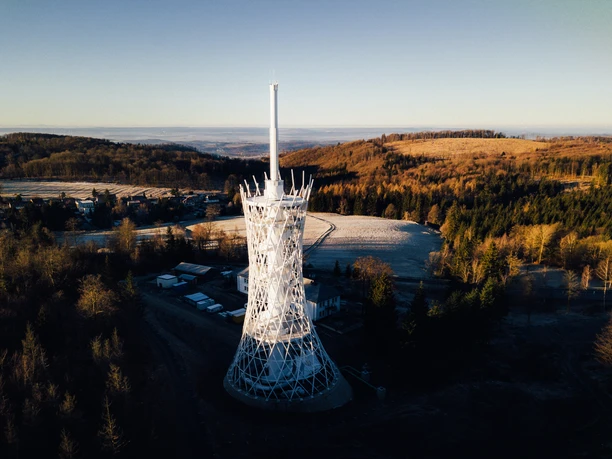 Blick auf die HEX Erlebniswelt von oben Moderner HEX Aussichtsturm in winterlicher Hügellandschaft mit Wald und weiten Ausblicken im Harz.
