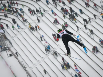 Sparkassen Vogtland Arena (c) Jan Simon Schäfer (1).jpg Ein Skispringer fliegt über die schneebedeckte Zuschauertribüne einer Sprungschanze.A ski jumper flies over the snow-covered grandstand of a ski jump.Skokan na lyžích letí nad zasněženou tribunou skokanského můstku.Skoczek narciarski przelatuje nad pokrytą śniegiem trybuną skoczni narciarskiej.Een schansspringer vliegt over de besneeuwde tribune van een skischans.Un saltatore con gli sci vola sopra la tribuna innevata di un trampolino.
