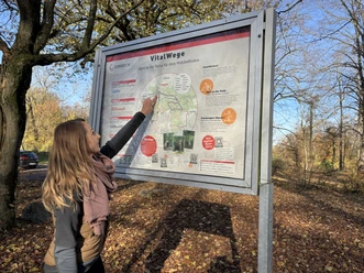 Vrouw kijkt naar het startbord van de vitaliteitspaden op de Hube in Einbeck in het herfstbos.