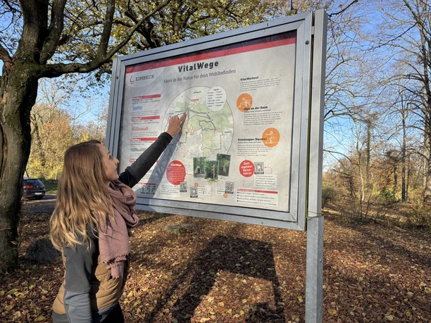 Vrouw kijkt naar het startbord van de vitaliteitspaden op de Hube in Einbeck in het herfstbos.