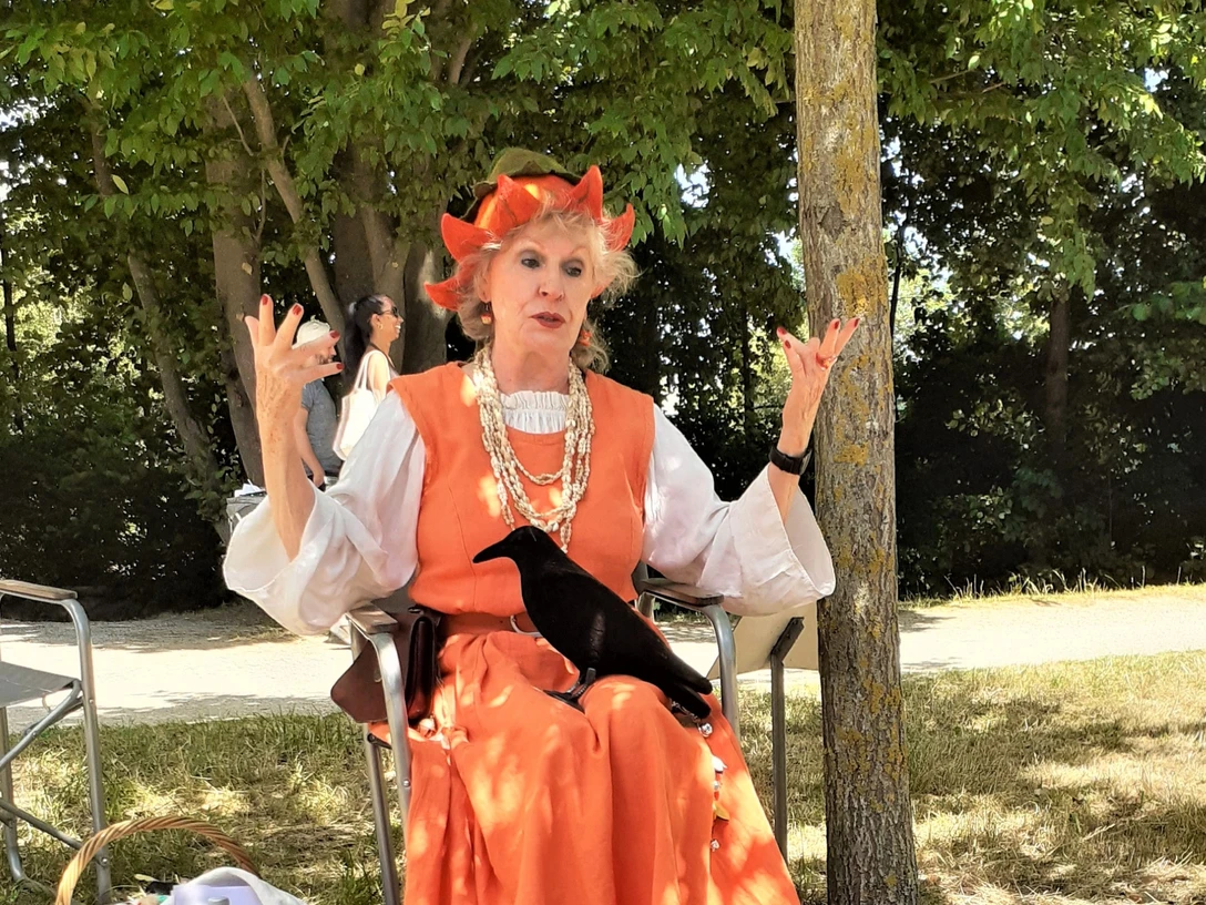 Eine Frau sitzt mit einem Raben auf dem Schoß vor einer Gruppe Kinder.