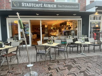 Titelbild.jpg Außenansicht des Stadtcafé Aurich mit Tischen und Stühlen auf der gepflasterten Terrasse.