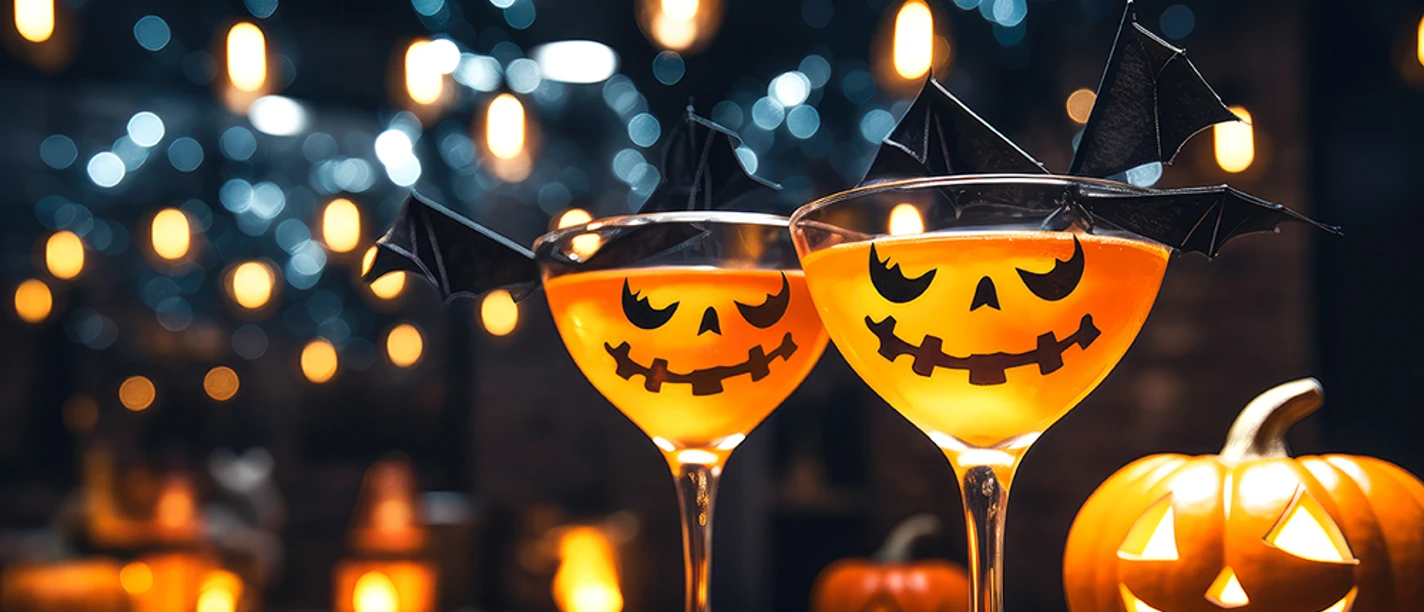 glas-kuerbis-halloween-party.jpg Zwei Halloween-Cocktails in Gläsern mit Kürbisfratzen, umgeben von Kerzenlicht.