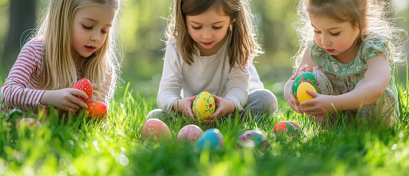 kind-ostereier-fruehling-wiese.jpg Drei kleine Mädchen sammeln bunte Ostereier im grünen Gras unter hellen Sonnenstrahlen.