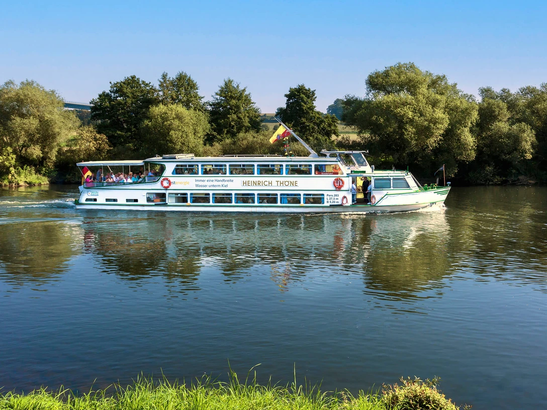 Weiße Flotte, Mülheim an der Ruhr Ein Ausflugsschiff fährt auf einem ruhigen Fluss, umgeben von grünen Bäumen.