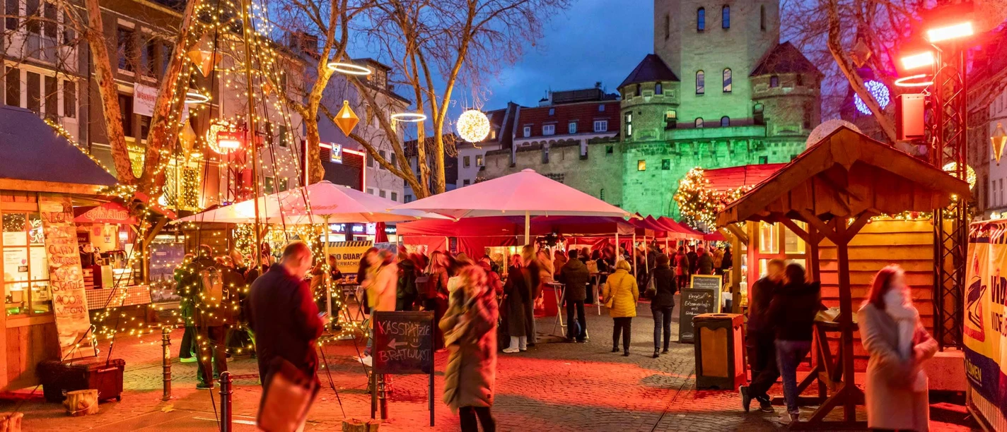 Christmas market on Chlodwigplatz in Cologne at dusk, with stalls, lights and people visiting.