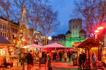 Weihnachtsmarkt auf dem Chlodwigplatz Weihnachtsmarkt auf dem Chlodwigplatz in Köln bei Abenddämmerung, mit Ständen, Lichtern und besuchenden Menschen.