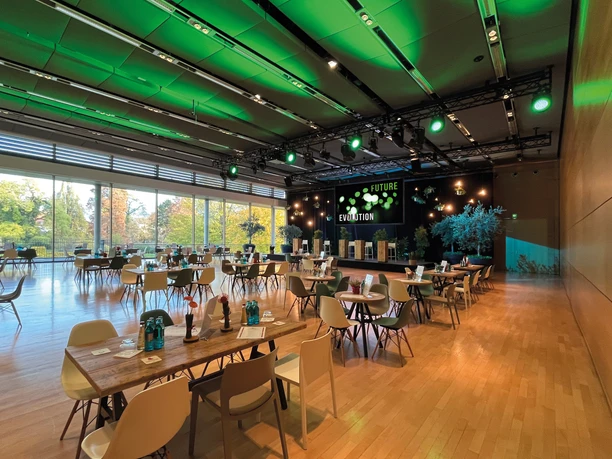 Congress Park Hanau - Saal Saal mit Tischen, Bühne und grüner Beleuchtung.
