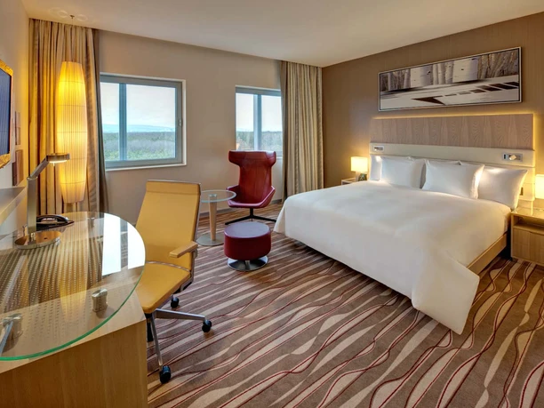 Hilton Frankfurt Airport - Hotelzimmer Modernes Hotelzimmer mit Bett, Schreibtisch und Sessel.