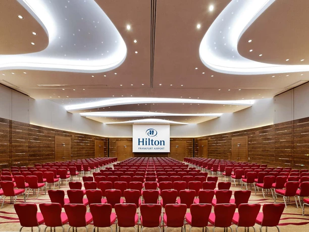Hilton Frankfurt Airport - Ballsaal Globe Großer Saal mit roten Stühlen und Wellendecke.