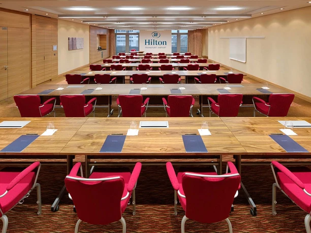 Hilton Frankfurt Airport - Conference room Conference room with red chairs and wooden tables.