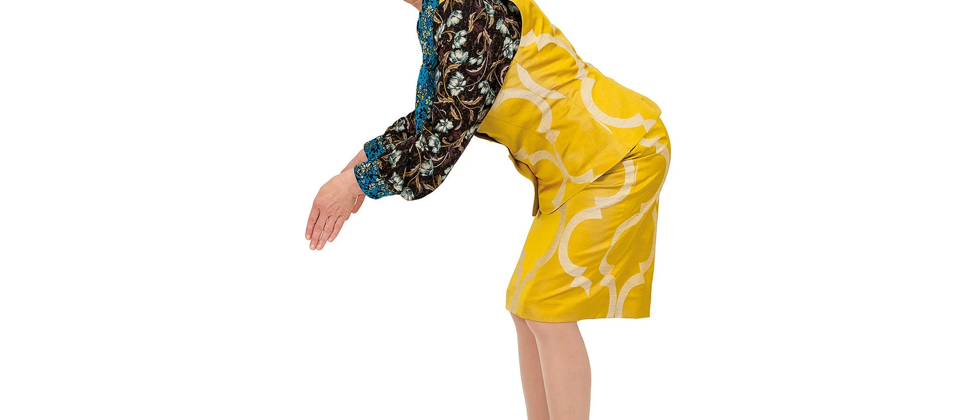 Frieda Braun_Jetzt oder nie_(c) Britta Schuessling.jpg Frau in gelbem Kleid mit gemusterten Ärmeln beugt sich humorvoll vor und blickt mit Brille zur Seite.