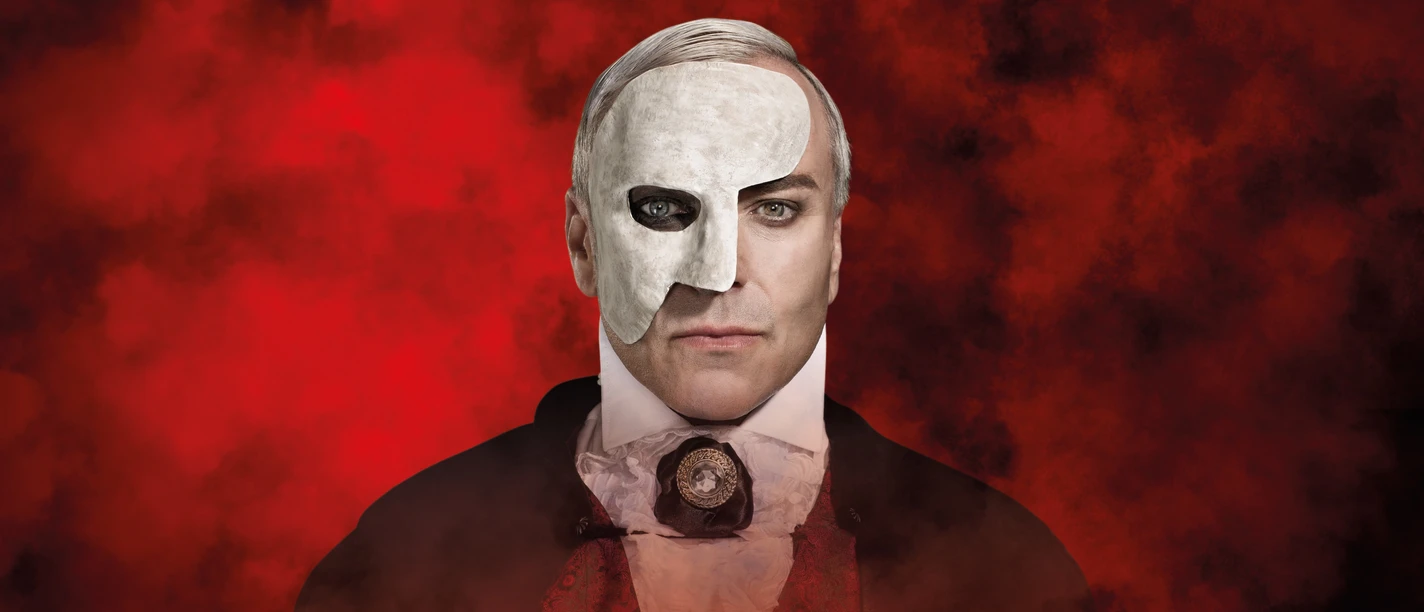 Foto Phantom Hauptfoto (C) Susannah Vergau.jpg Mann mit weißer Halbmaske vor rotem Nebelhintergrund, in eleganter viktorianischer Kleidung.