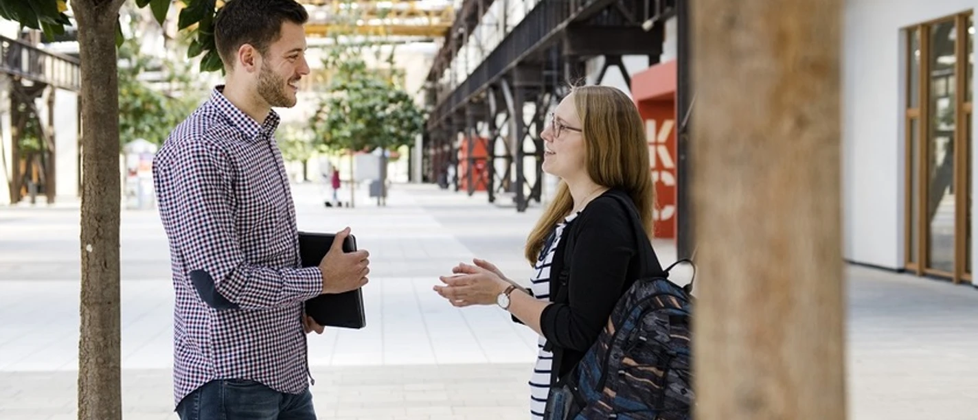 Bild.jpeg Zwei Studierende unterhalten sich im modernen Innenhof der Hochschule Osnabrück.