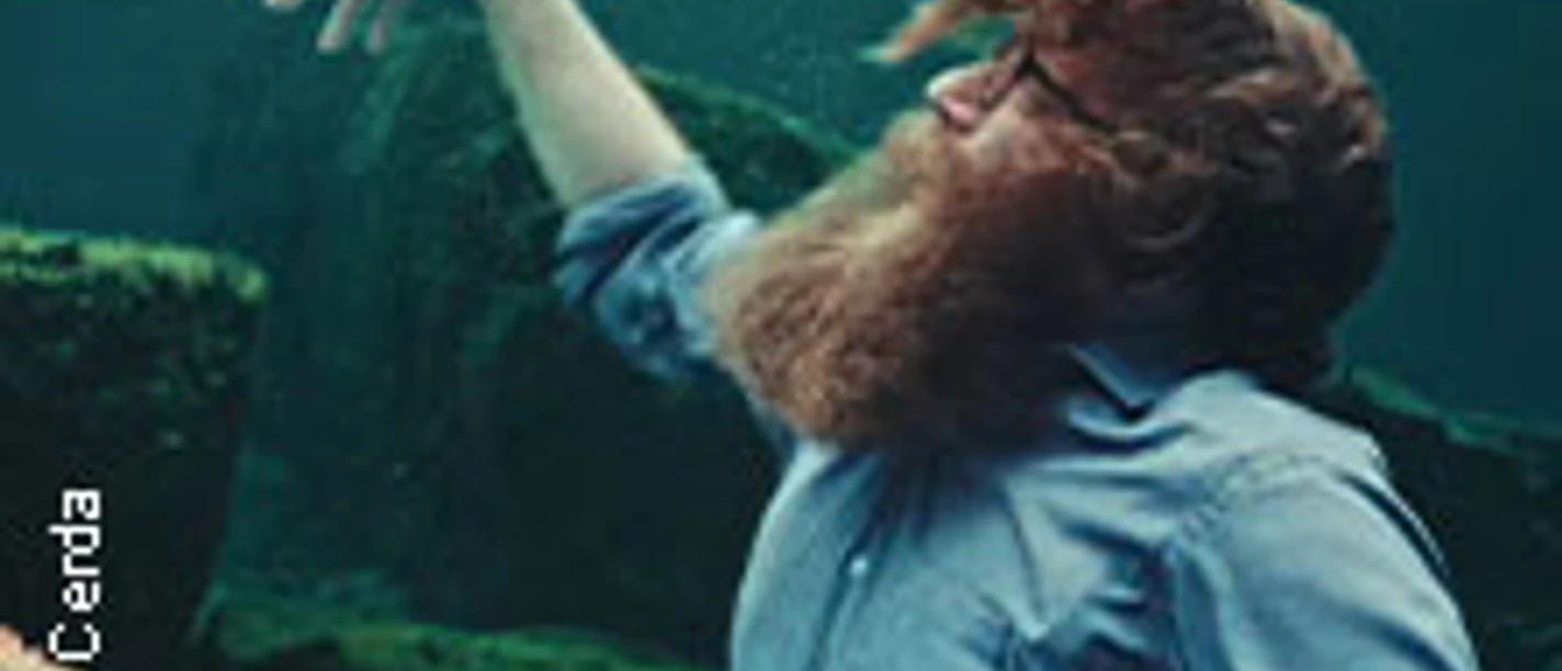 Der Musiker Ben Caplan, mit voller Bartpracht, unter Wasser in einer kreativen Pose.