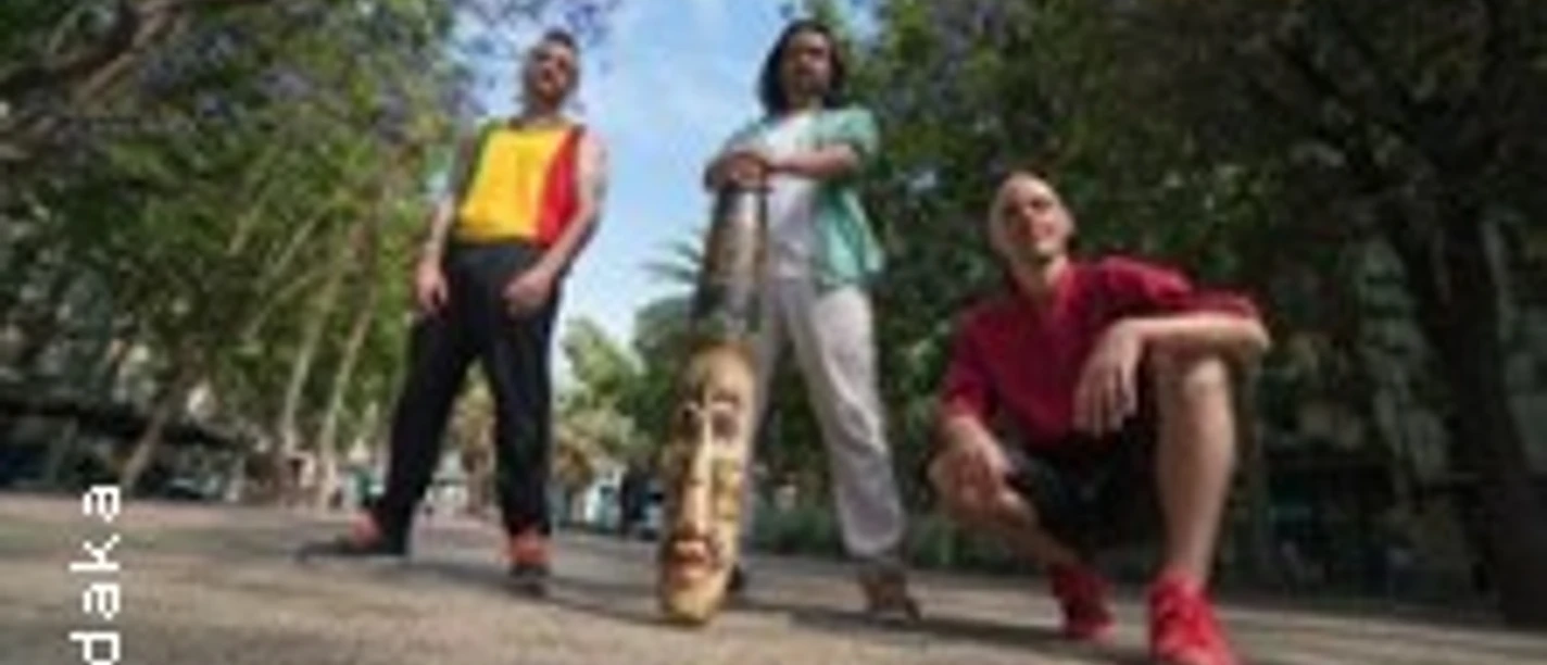 Drei Personen posieren draußen bei einem Spaziergang auf einem baumbestandenen Platz.