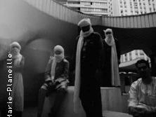 Gruppe von Musiker:innen in traditioneller Kleidung unter freiem Himmel vor Hochhäusern.