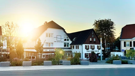 Hotel Restaurant zum Vater Rhein Hotel Restaurant Zum Vater Rhein. Hell gestrichenes Gebäude, im Sonnenlicht leuchtend, mit Außengastronomie am Rhein.