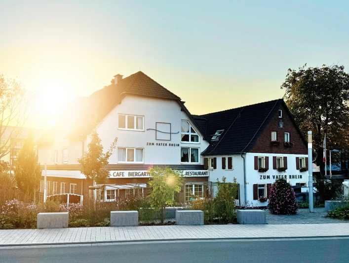 Hotel Restaurant zum Vater Rhein Hotel Restaurant Zum Vater Rhein. Hell gestrichenes Gebäude, im Sonnenlicht leuchtend, mit Außengastronomie am Rhein.